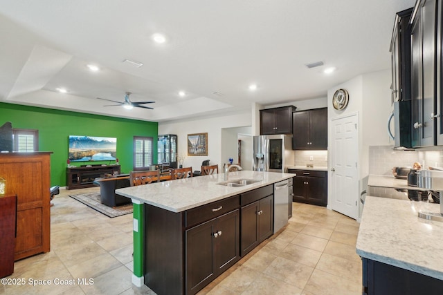 kitchen featuring sink, a center island with sink, a tray ceiling, stainless steel appliances, and light stone countertops