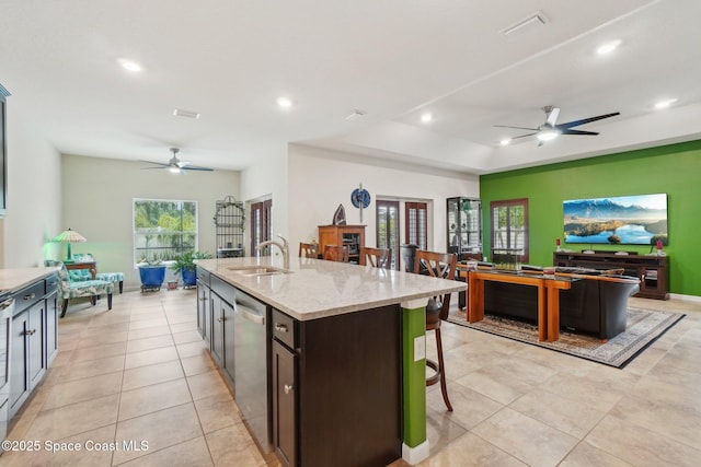 kitchen featuring an island with sink, dishwasher, sink, a kitchen breakfast bar, and light stone counters