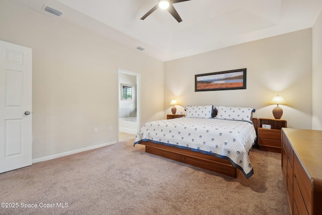 bedroom featuring a raised ceiling, ceiling fan, light carpet, and ensuite bath