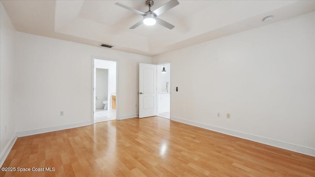 empty room featuring ceiling fan, light hardwood / wood-style flooring, and a raised ceiling