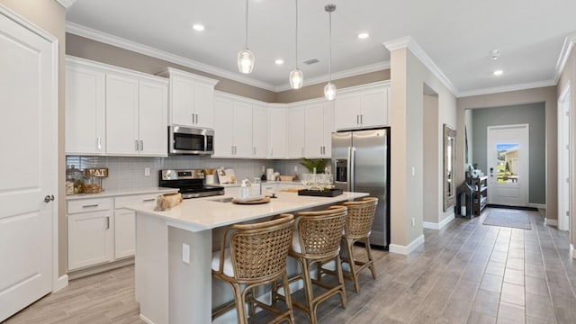 kitchen with a kitchen island with sink, stainless steel appliances, a breakfast bar, white cabinets, and decorative light fixtures