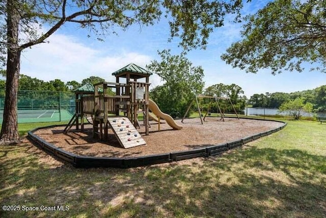 view of jungle gym featuring tennis court, a yard, and a water view