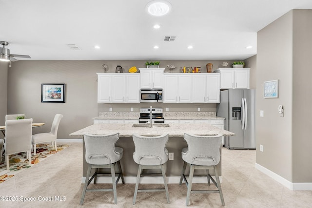 kitchen featuring stainless steel appliances, white cabinetry, a center island with sink, and light stone countertops