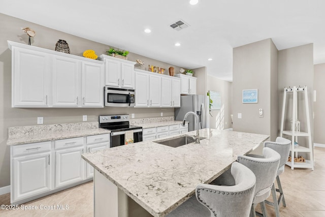 kitchen with sink, white cabinetry, light stone countertops, a kitchen island with sink, and stainless steel appliances