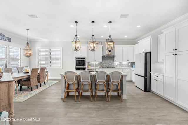 kitchen featuring white cabinetry, stainless steel double oven, fridge, a kitchen island with sink, and pendant lighting