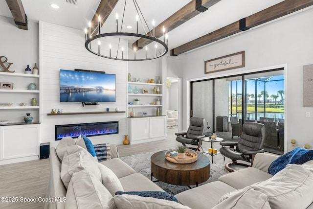 living room featuring beam ceiling, a large fireplace, built in features, and light wood-type flooring