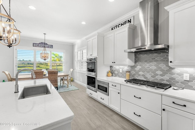 kitchen featuring sink, hanging light fixtures, stainless steel appliances, white cabinets, and wall chimney exhaust hood