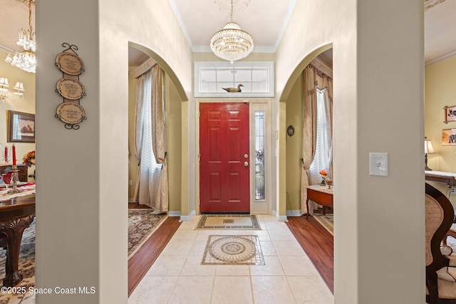 tiled foyer with crown molding and an inviting chandelier