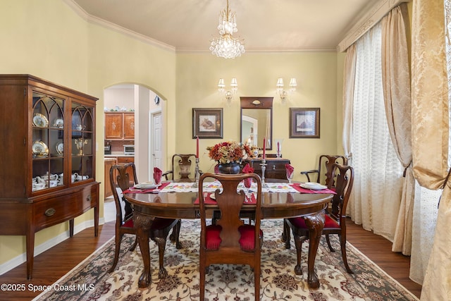 dining space featuring dark wood-type flooring, ornamental molding, and a notable chandelier