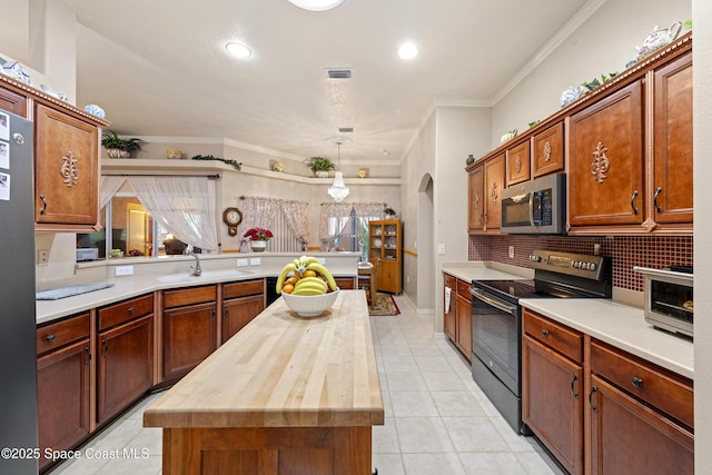 kitchen with wood counters, a kitchen island, stainless steel appliances, sink, and hanging light fixtures