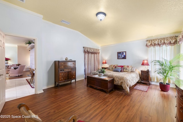 bedroom featuring vaulted ceiling, a textured ceiling, crown molding, and hardwood / wood-style floors