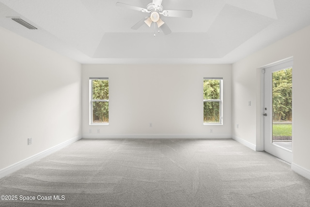 empty room featuring ceiling fan, light carpet, and a raised ceiling