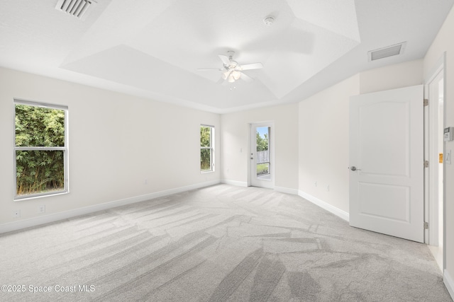 carpeted spare room with ceiling fan, a wealth of natural light, and a tray ceiling