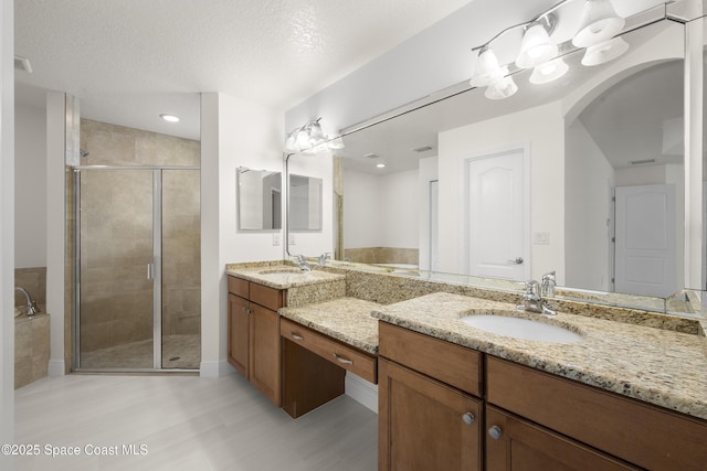 bathroom featuring a textured ceiling, a shower with door, and vanity