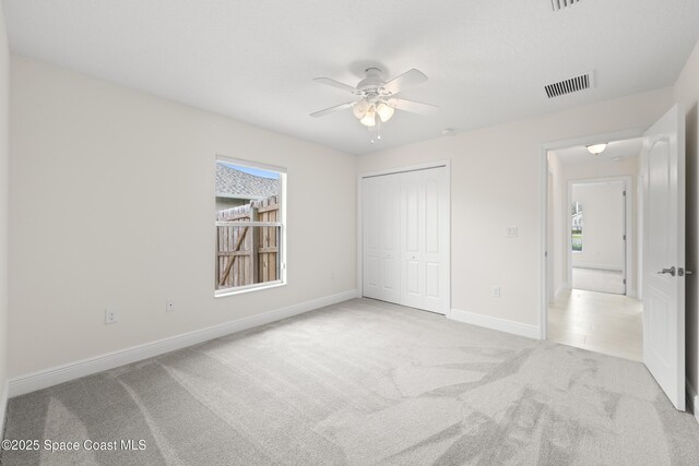 unfurnished bedroom featuring ceiling fan, light colored carpet, multiple windows, and a closet