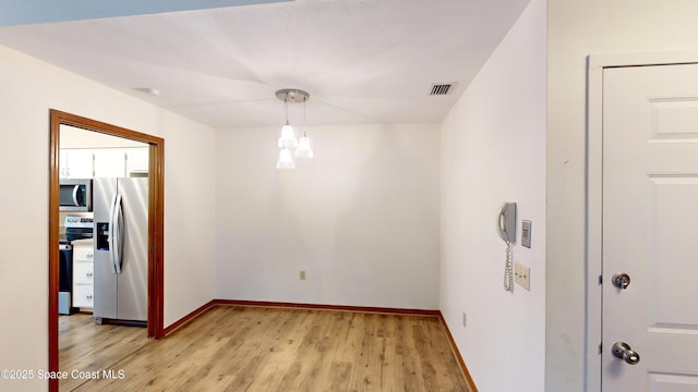 spare room with light wood-type flooring and a notable chandelier