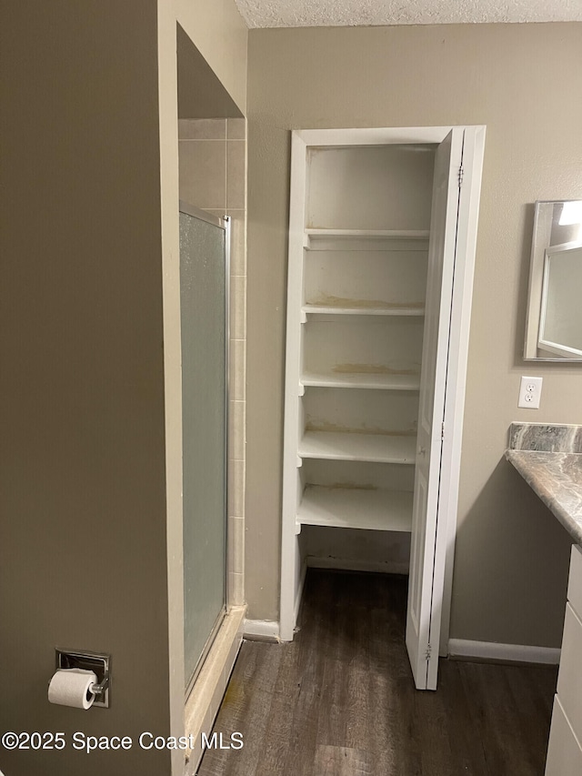 bathroom featuring a textured ceiling, wood-type flooring, walk in shower, and vanity