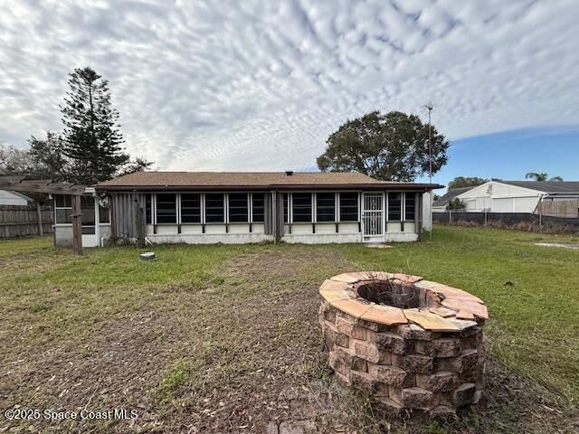 rear view of house with an outdoor fire pit, a sunroom, and a lawn