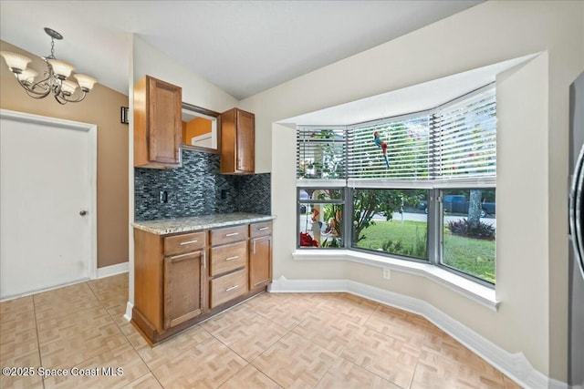 kitchen featuring light stone countertops, decorative backsplash, hanging light fixtures, a chandelier, and vaulted ceiling