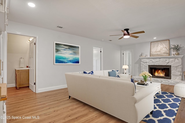 living room featuring ceiling fan, light hardwood / wood-style floors, and a stone fireplace