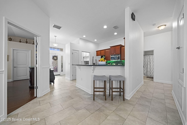 kitchen with light tile patterned floors, kitchen peninsula, a breakfast bar area, stainless steel appliances, and decorative light fixtures