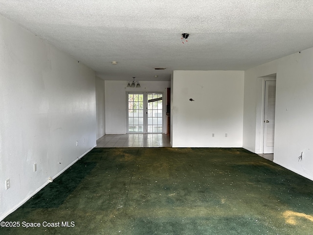 unfurnished room with a notable chandelier, french doors, carpet, and a textured ceiling