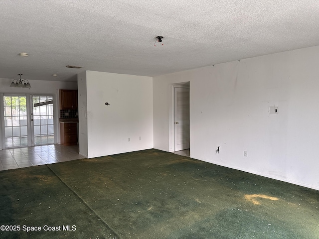 empty room with french doors, carpet flooring, a textured ceiling, and a notable chandelier