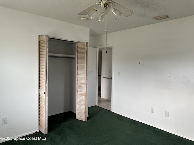 unfurnished bedroom with a closet, ceiling fan, a textured ceiling, and dark colored carpet