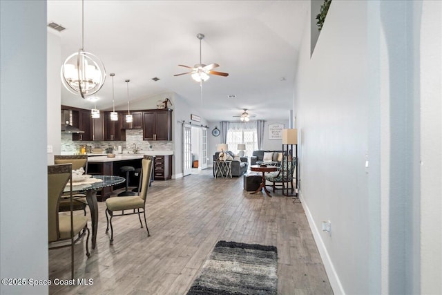 dining area featuring lofted ceiling, light wood-type flooring, sink, and ceiling fan with notable chandelier