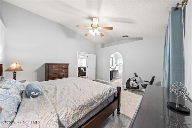 bedroom with a textured ceiling, vaulted ceiling, ensuite bath, light wood-type flooring, and ceiling fan