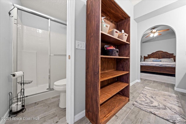 bathroom featuring a shower with shower door, ceiling fan, and toilet