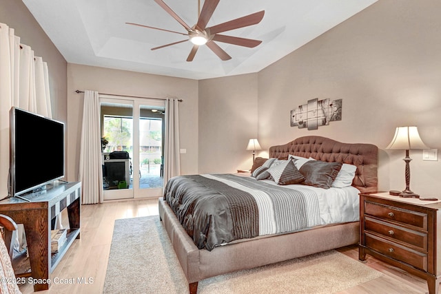 bedroom with ceiling fan, light hardwood / wood-style floors, a raised ceiling, and access to outside