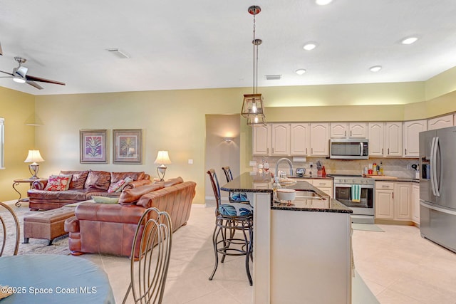 kitchen with stainless steel appliances, a kitchen breakfast bar, dark stone counters, hanging light fixtures, and sink