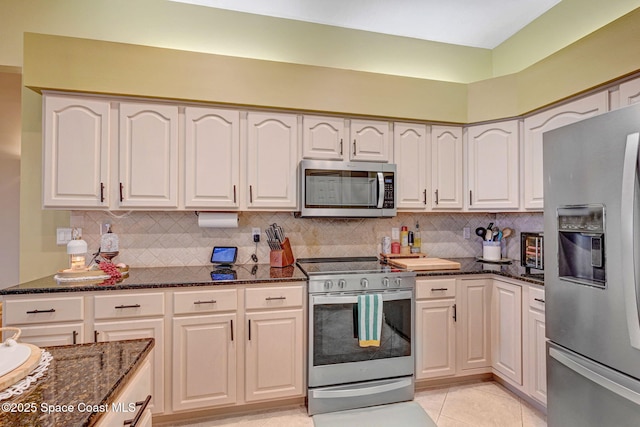 kitchen with light tile patterned floors, appliances with stainless steel finishes, tasteful backsplash, and dark stone countertops