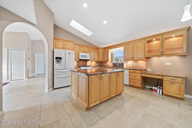 kitchen featuring a center island, white appliances, a skylight, backsplash, and dark stone counters