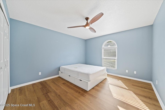 unfurnished bedroom with wood-type flooring, a closet, ceiling fan, and a textured ceiling