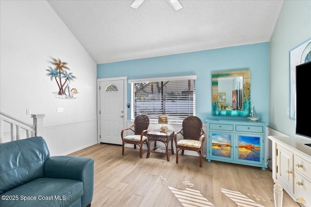 living area with lofted ceiling, a textured ceiling, ceiling fan, and light hardwood / wood-style floors