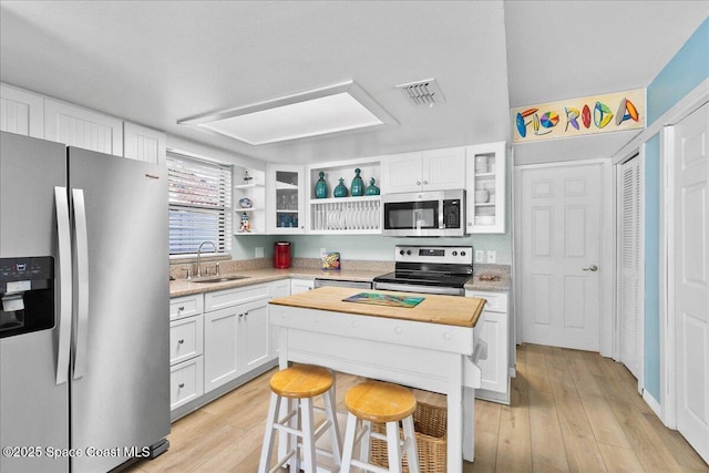 kitchen with stainless steel appliances, sink, white cabinetry, light hardwood / wood-style flooring, and a breakfast bar