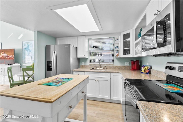 kitchen with stainless steel appliances, sink, white cabinetry, light hardwood / wood-style floors, and a kitchen island