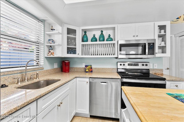 kitchen featuring white cabinets, appliances with stainless steel finishes, light stone countertops, and sink