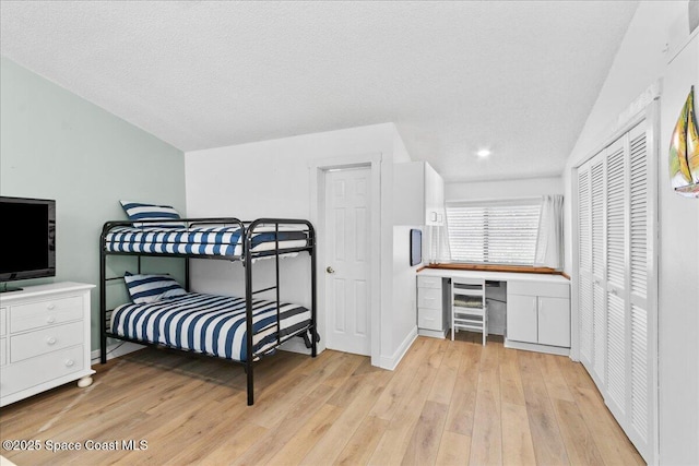 bedroom with a closet, light hardwood / wood-style floors, built in desk, a textured ceiling, and lofted ceiling