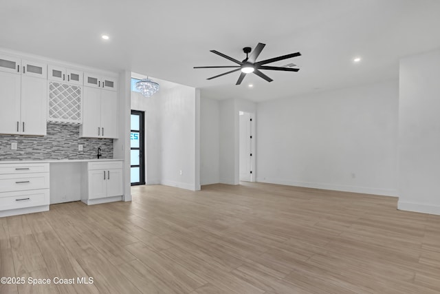 unfurnished living room featuring sink, ceiling fan with notable chandelier, and light wood-type flooring