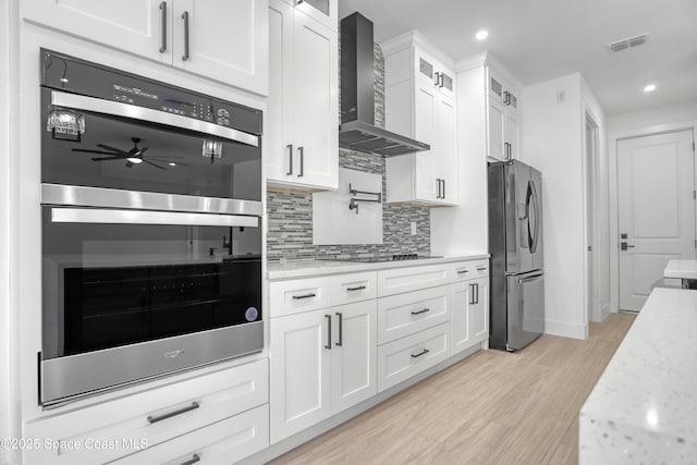 kitchen with appliances with stainless steel finishes, white cabinets, light stone counters, and wall chimney exhaust hood