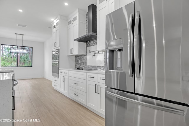 kitchen featuring white cabinetry, wall chimney range hood, light stone counters, and stainless steel appliances