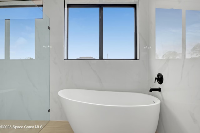 bathroom with a tub to relax in and tile walls