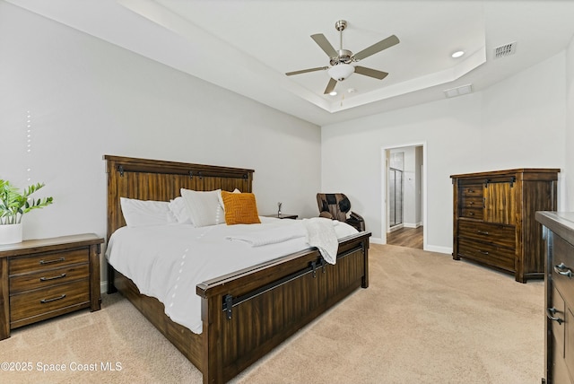 bedroom featuring connected bathroom, light carpet, ceiling fan, and a tray ceiling