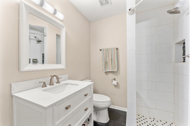 bathroom featuring a tile shower, vanity, and toilet