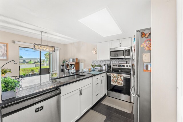 kitchen with appliances with stainless steel finishes, kitchen peninsula, sink, white cabinetry, and backsplash