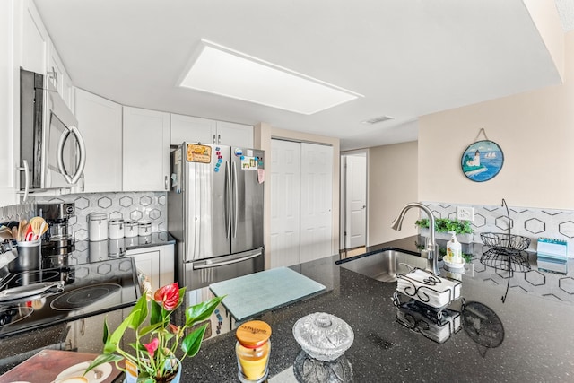 kitchen with stainless steel appliances, tasteful backsplash, white cabinets, dark stone counters, and sink