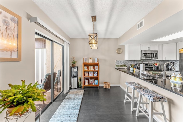 interior space with hanging light fixtures, stainless steel appliances, decorative backsplash, white cabinetry, and dark stone counters